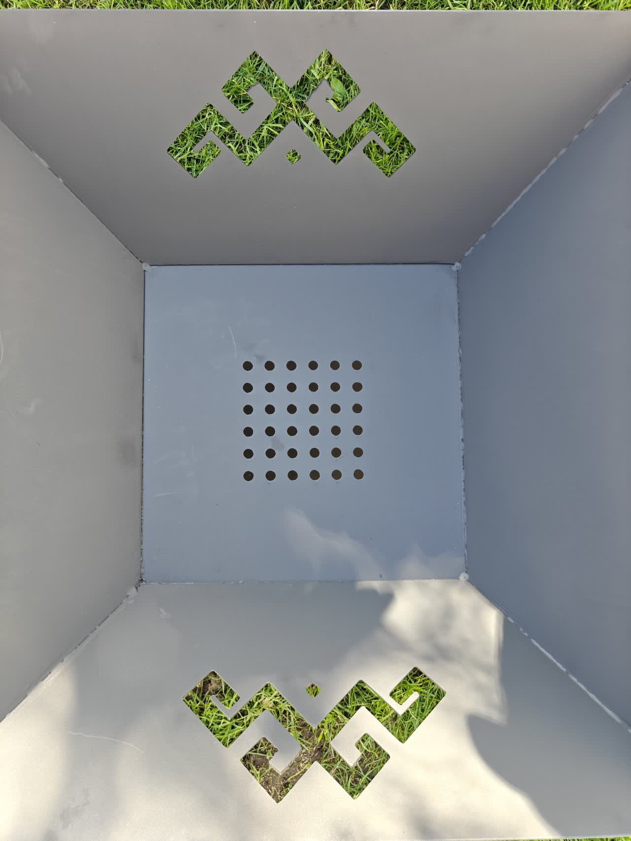 Birds-eye view of The Foco fire pit showing the central floor grate and matching cultural-inspired pattern cut-outs on the steel walls.